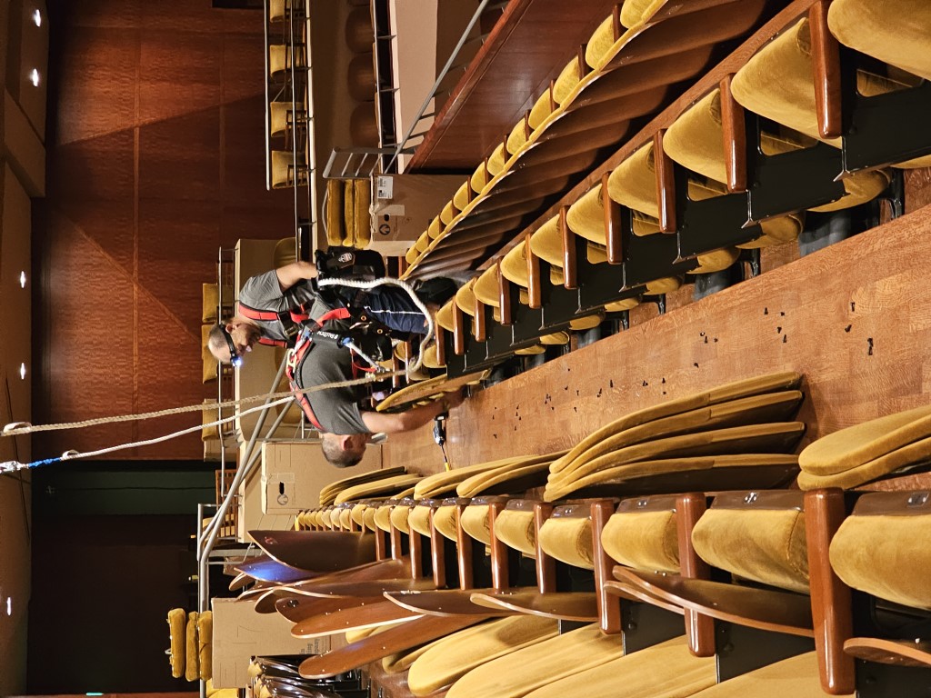 Upholsterers on the balcony wearing rigging while assembling newly upholstered seating